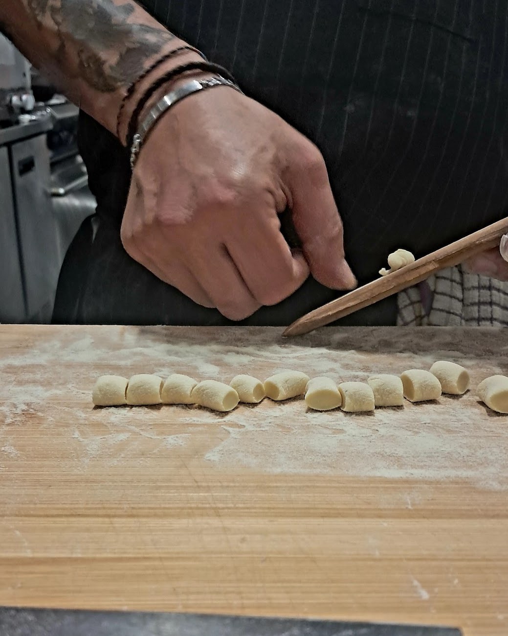 Two pairs of hands hand-rolling gnocchi on a floured wooden board in the kitchen at Bell Pesto Café.