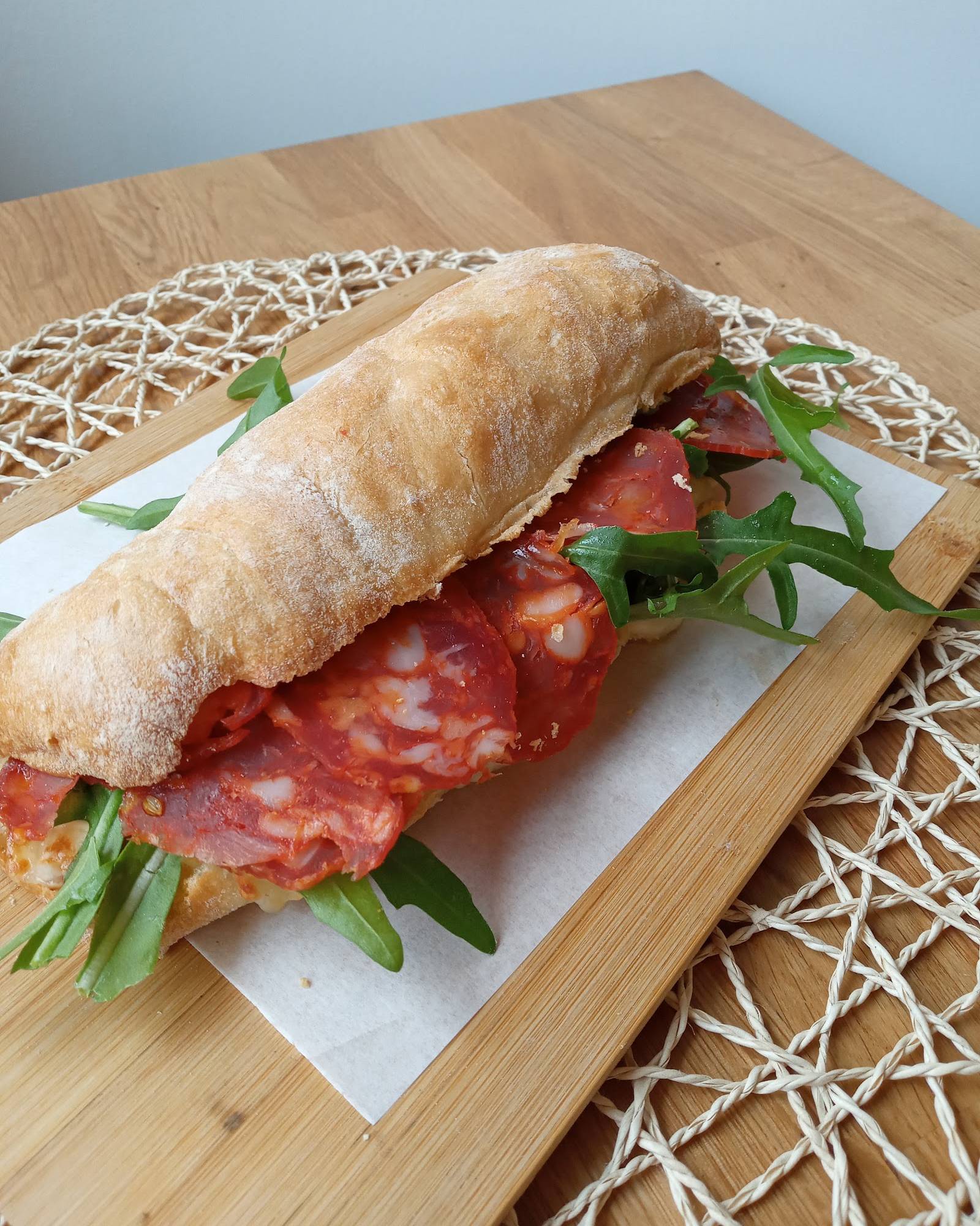 A chorizo and rocket panino on a wooden board with a woven placemat, at Bell Pesto Café.